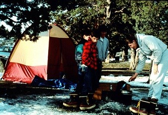 Two adults and two children near an unlit firepit and a tent.