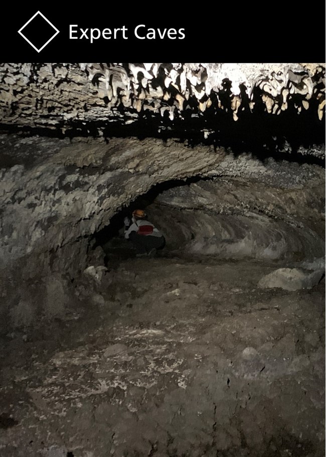 A tight cave passages with a caver crawling in the background