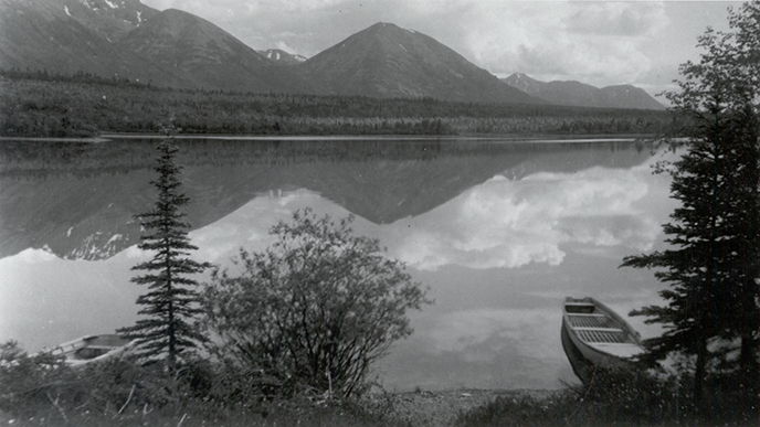 black and white photo looking across Hardenburg Bay towards Port Alsworth with Martha's Mountain reflecting in the water. No other buildings are in view.