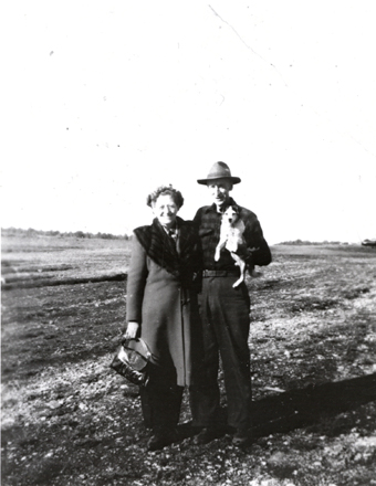 black and white image of a man and woman posing in a field, holding a small dog black and white image of a man and woman posing in a field, holding a small dog