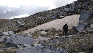 man walking on a rocky hillside near a patch of snow