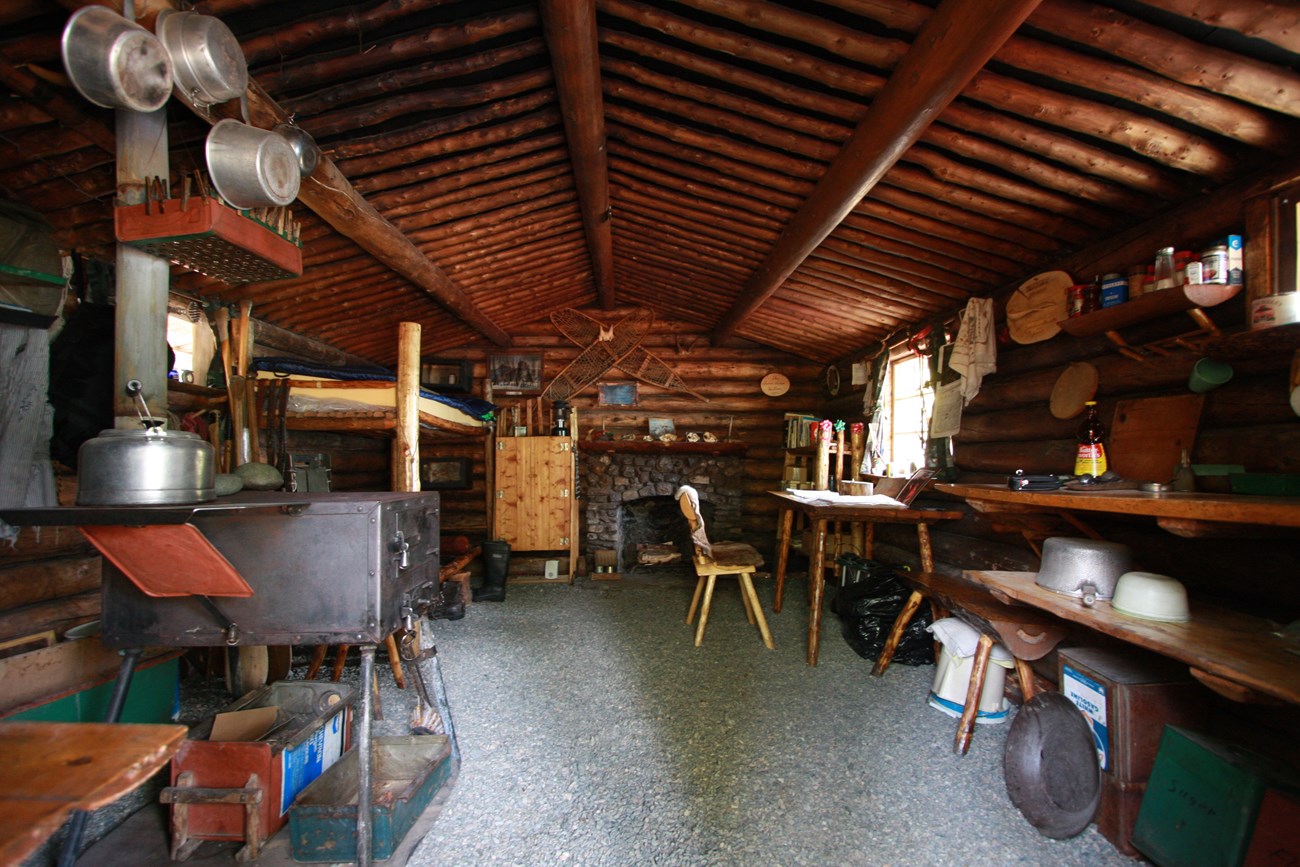 A wooden cabin interior with fireplace, wood stove, furniture and hanging pots