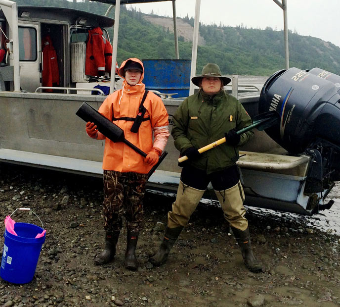 two woman with shovels standing on a beach near a boat two woman with shovels standing on a beach near a boat