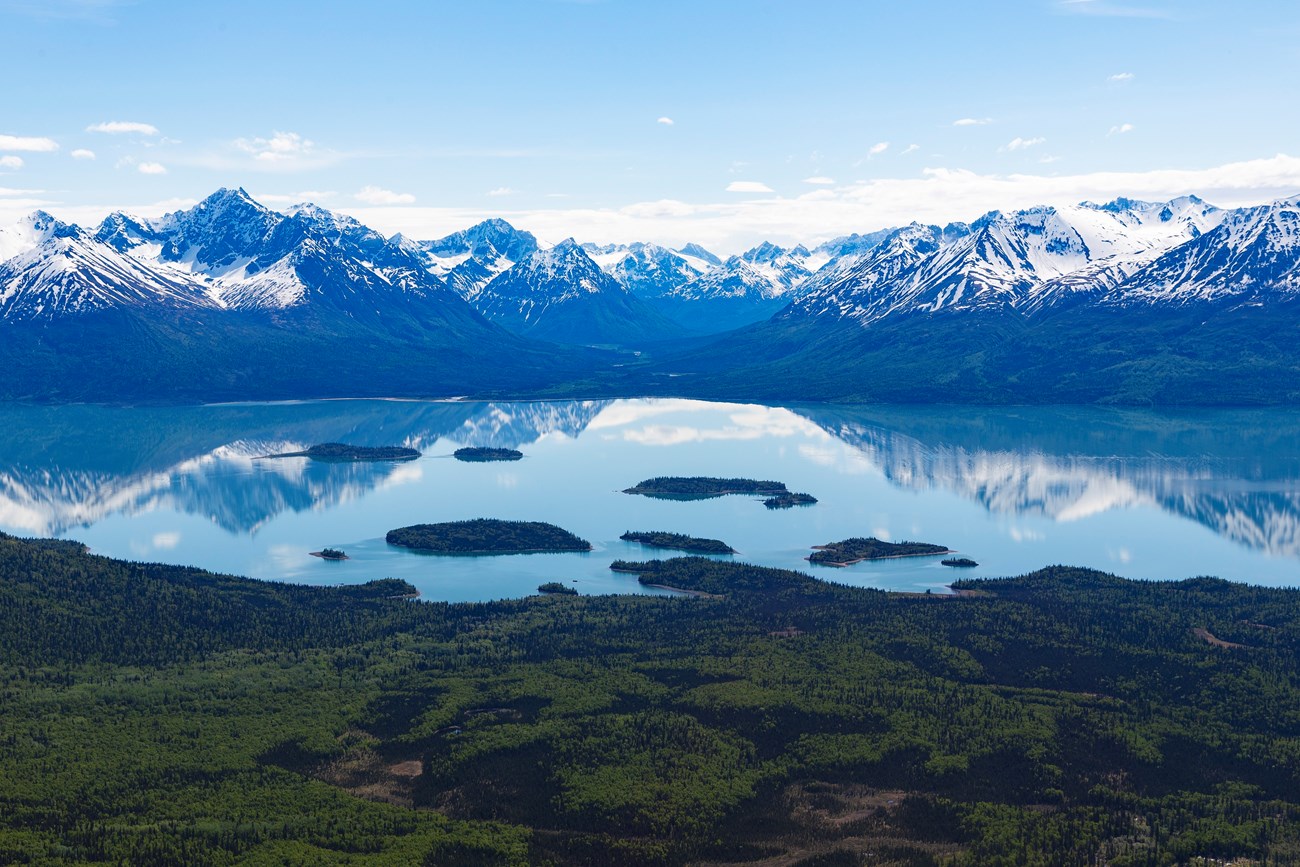 snow capped mountains reflect in the still blue water of Lake Clark