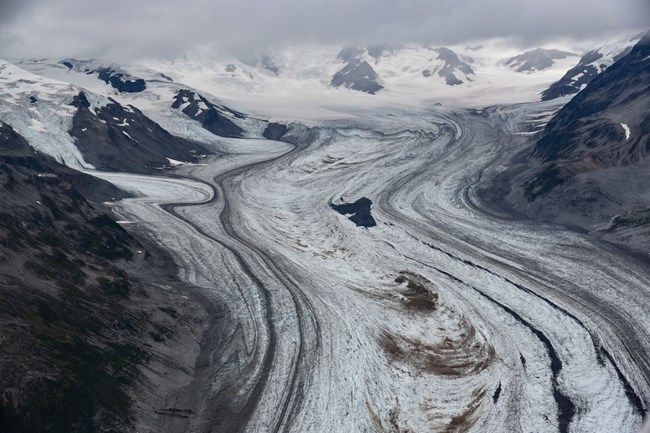Image of an ice field in high mountains, a glacier snakes down the center of the photograph.