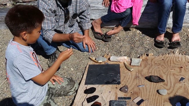 Young boy sits on ground holding tool.