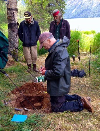 man kneeling by a shallow hole in the ground, two other men looking on