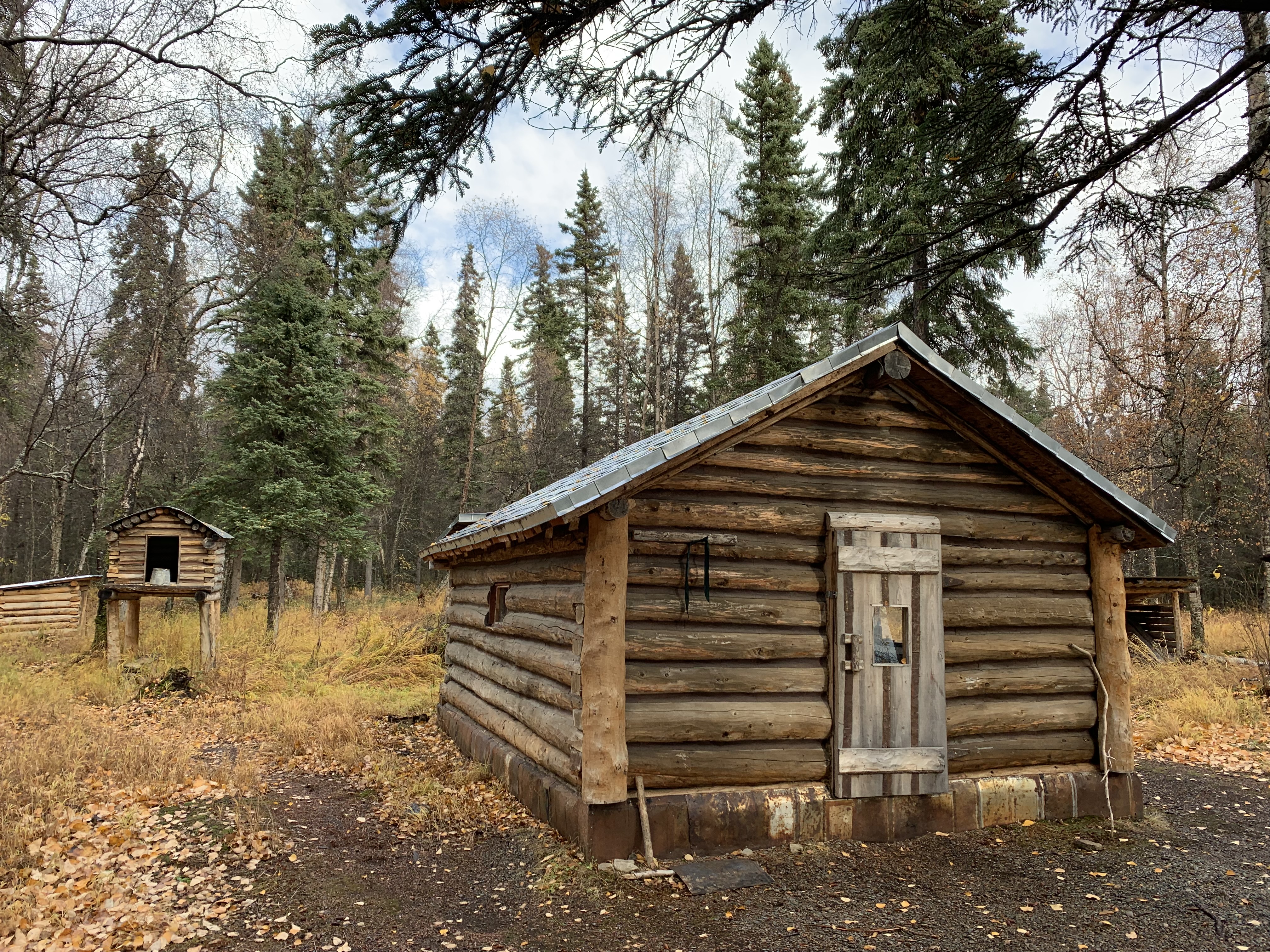 The Joe Thompson Cabin in autumn by NPS/K. Lewandowski a wooden cabin and a food cache in an autumn forest