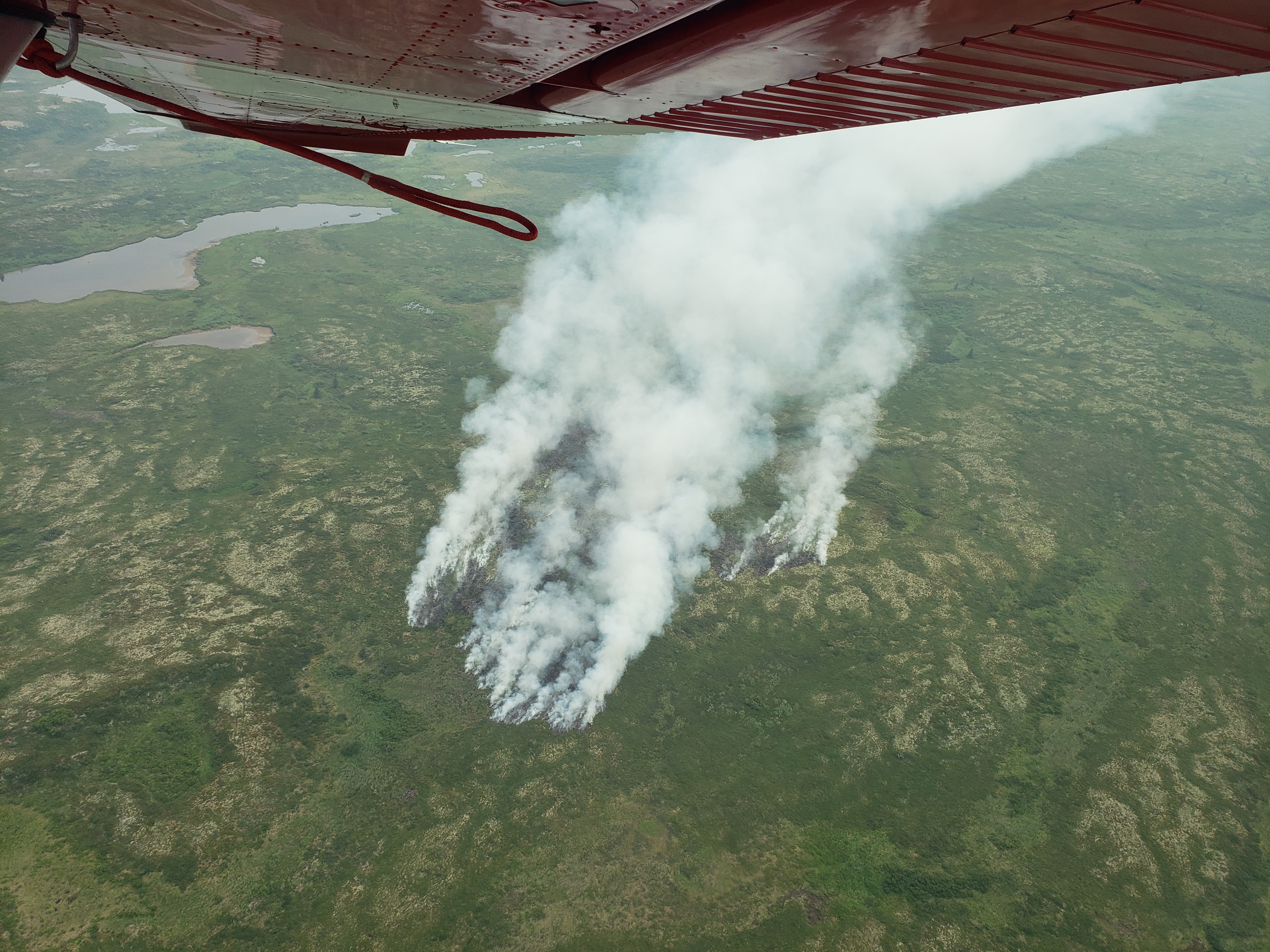 Shot from an airplane, smoke rises from green tundra. Shot from an airplane, smoke rises from green tundra.