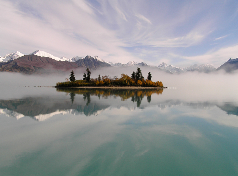 mist rising around a small island in a lake, with snowy mountains in the distance mist rising around a small island in a lake, with snowy mountains in the distance