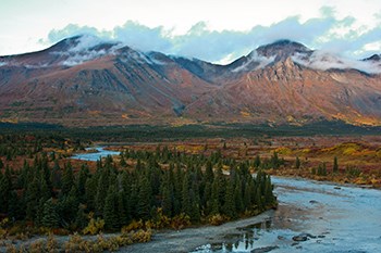 Photo of a river winding through forest with autumn colors and mountains in the distance