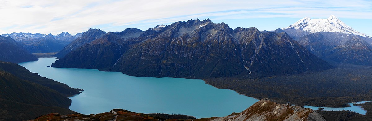 Aerial photo of a turquoise blue lake bounded by steep mountains.