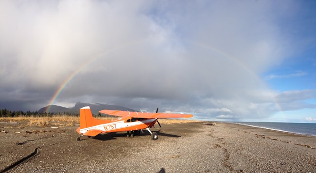 an orange plane on a beach with a rainbow overhead