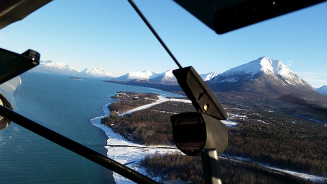 view from airplane, an ice covered airstrip, a blue lake and mountains