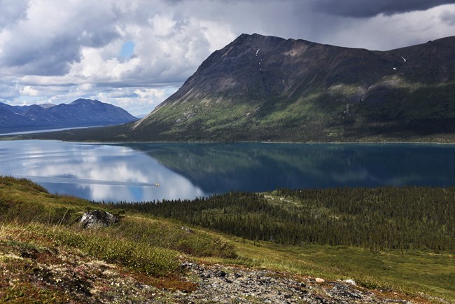 from a mountain, a yellow plane lands on a blue lake surrounded by mountains