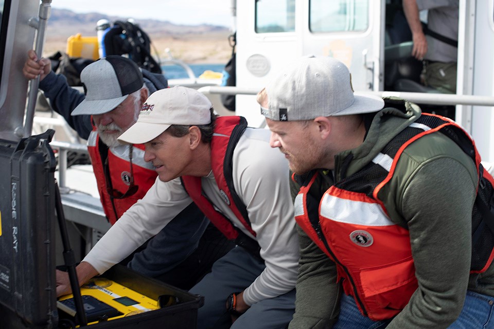 Three team participants wearing orange flotation vests examine project information.