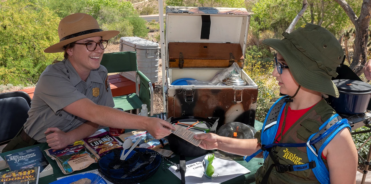 Junior Ranger shaking hands with park ranger at an activity booth. Junior Ranger shaking hands with park ranger