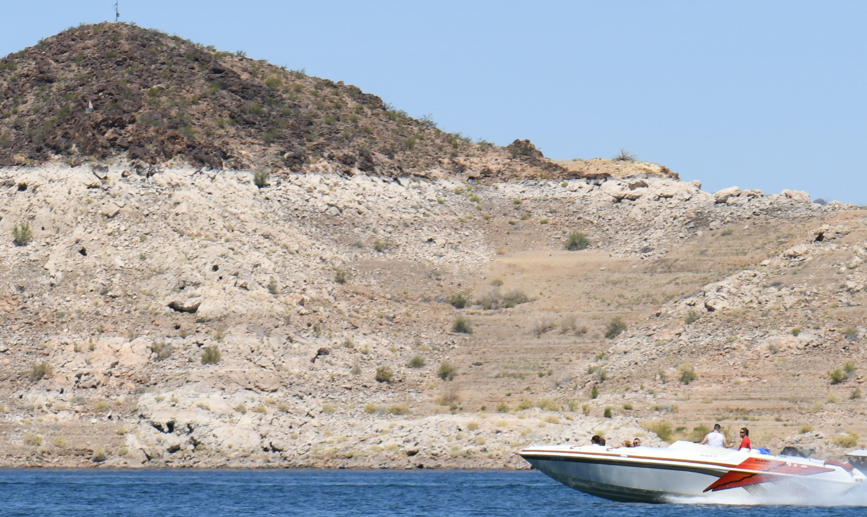 Speed boat on the water with change in color on shore that indicates how low from full pool the water level is.