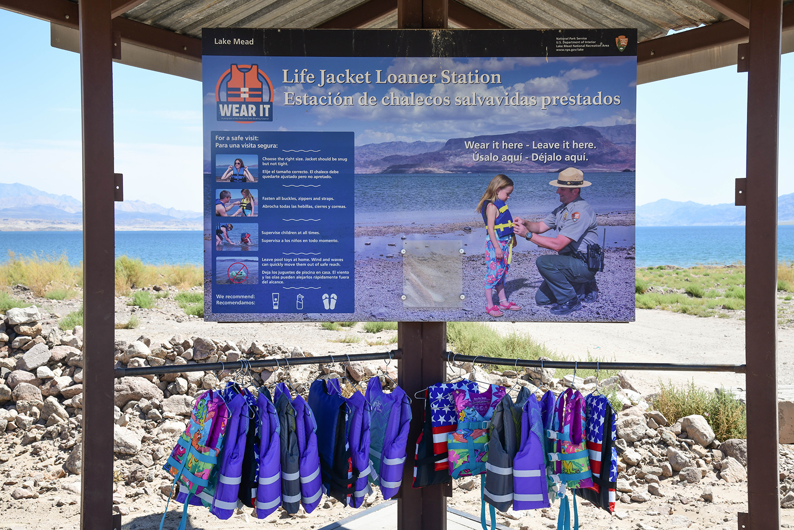 Lifejacket Loaner Station Boulder Beach Lake Mead kiosk with a sign and new life jackets hanging with water in the background