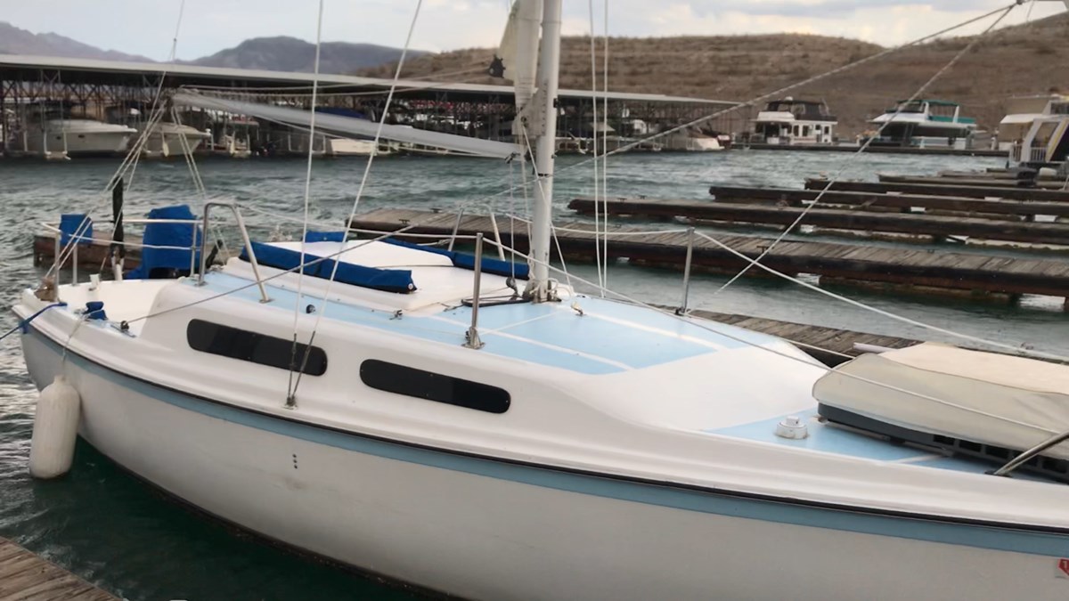 White sailboat with light blue trim is moored a slip in marina.