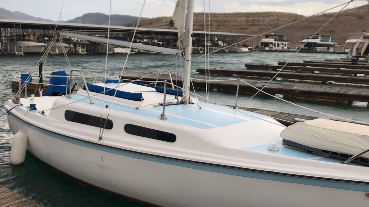 Yule Vessel White sailboat with light blue trim is moored a slip in marina.