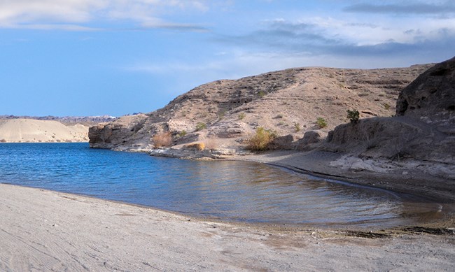 Photo of calm water surrounded by hills on right and smooth beach on left