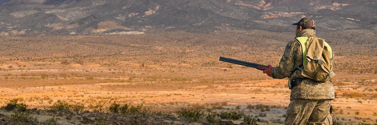 Camouflaged hunter with rifle in open desert