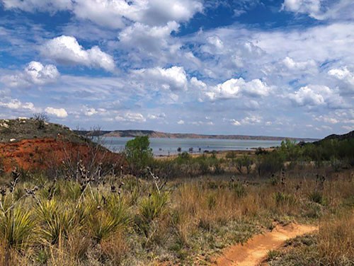 Harbor Bay Trail with view of Lake Meredith on a sunny day.  The trail is reddish-orange layered with Permian dirt.