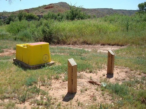 Automatic self-filling horse water tank at Plum Creek campgrounds.  It is a sunny day with blue skies.  The horse water tank is yellow.  There is a mesa in the background covered with vegetation.