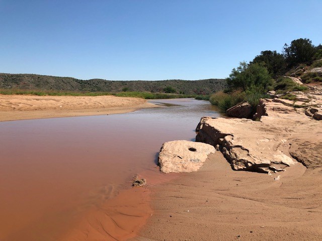 The Canadian River running through Rosita Flats area.  The river is a orange with a white rock near the shore.
