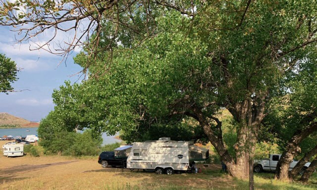 Cedar Canyon Campgrounds with campers underneather big cottonwoods.  There is a view of the lake and the sky is blue.