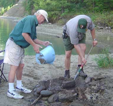 Volunteer and ranger putting out an unattended fire. Volunteer is pouring water over the pit and the ranger is putting sand in the pit. Volunteer and ranger putting out an unattended fire. Volunteer is pouring water over the pit and the ranger is putting sand in the pit.