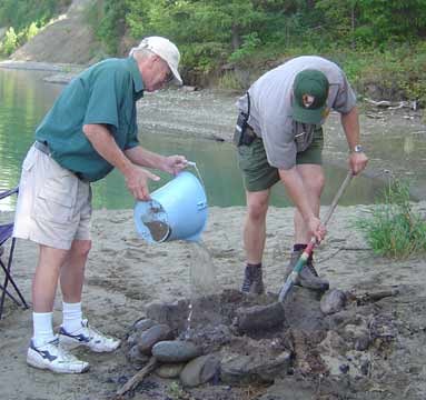 Volunteer and ranger putting out an unattended fire. Volunteer is pouring water over the pit and the ranger is putting sand in the pit.