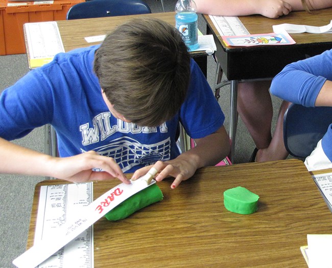 Student making scale models of planets. A student uses play dough to make scale models of planets.