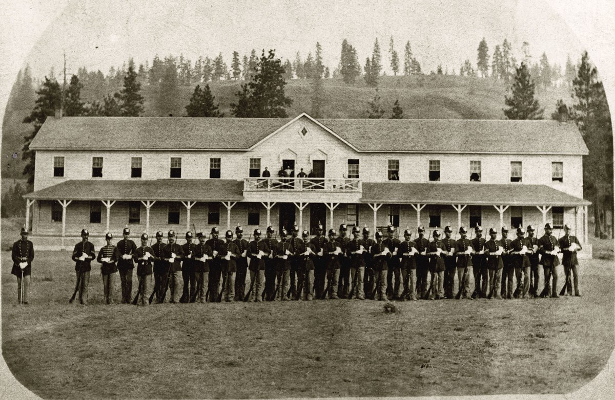 historic photo of soldiers in dress uniform lined up in front of barracks
