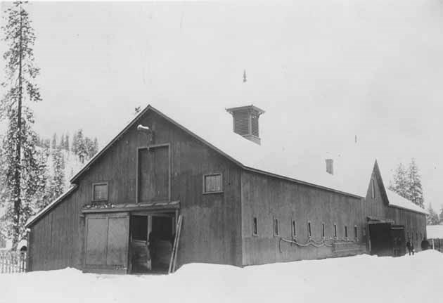 Fort Spokane. Historic photo of quartermaster's barn. Long 2 story barn in snow. Two man at the far end.
