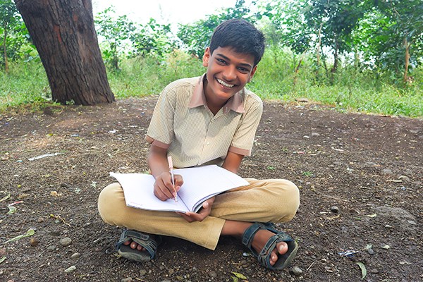 A boy sits cross-legged on the ground writing in a journal.