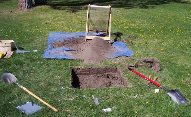 Archeology tools, screen, shovel, blue tarp around a square hole. Archeology tools, screen, shovel, blue tarp around a square hole.