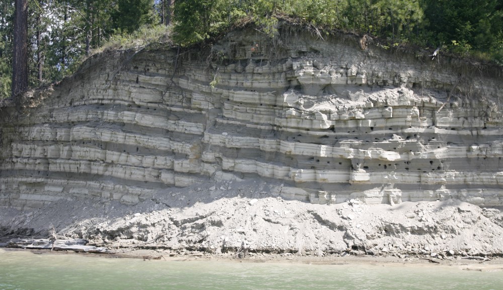 A 20ft high bank along a lake. Sediments are exposed in alternating light and dark layers. 