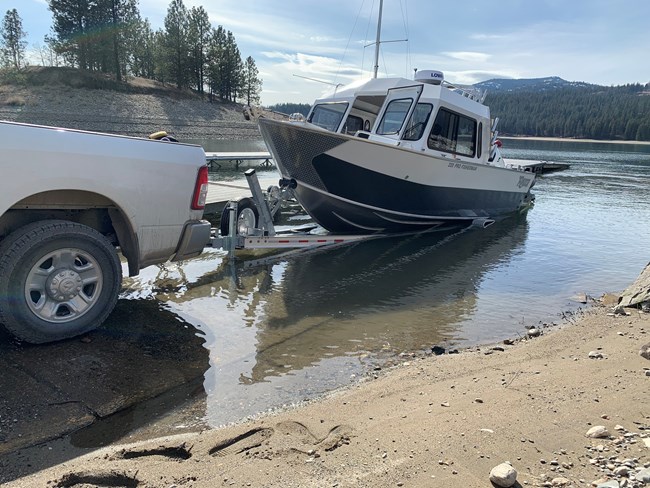 a boat on a trailer attached to a white truck is put into the water at a boat launch