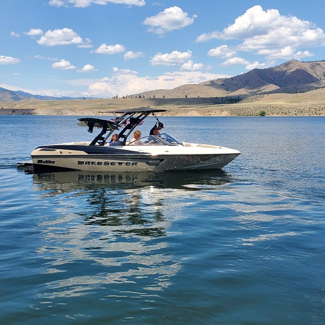 White and tan boat sits on glassy reflective blue water with dried hills in the background.