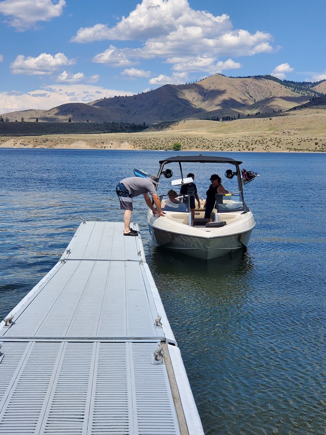 a family loads onto a small boat on a dock. A man stands on the dock leaning down to the boat while his family sits in the boat