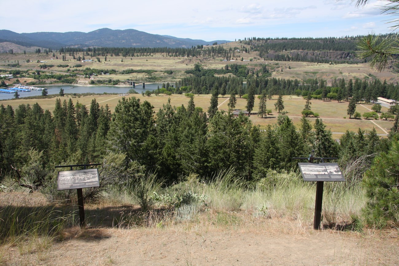 Two informational signs in front of a sweeping view of a fort.