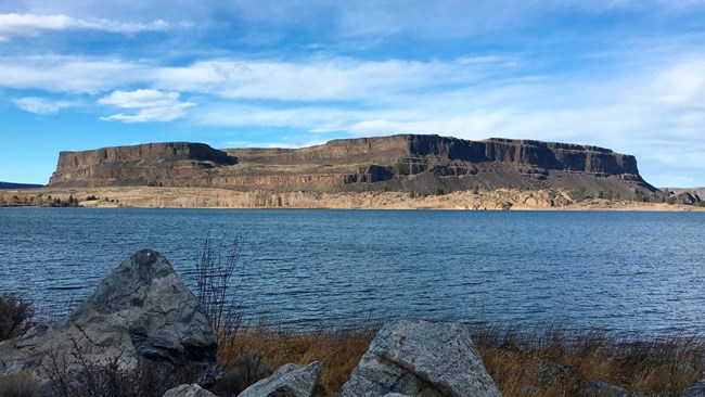 Large flat mountain with angular variation beyond a blue body of water.