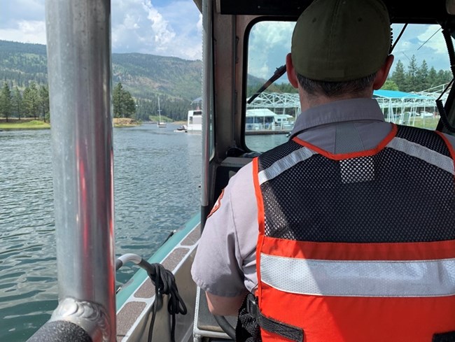 Park ranger with a orange life vest navigates on a boat.