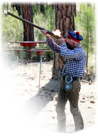 Member of Friends of Spokane House fires a black power musket. Dressed in buckskin trousers, blue checked shirt and Scottish bonnet