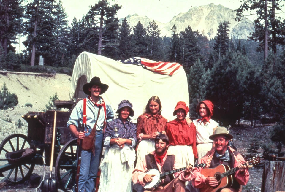 A group of four women and three men in front of a cloth-covered, wooden wagon