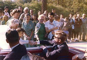 A man seated in a convertible shakes a boys hand amid a crowd
