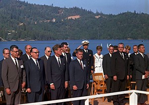 A group of men in suites backed by a blue lake