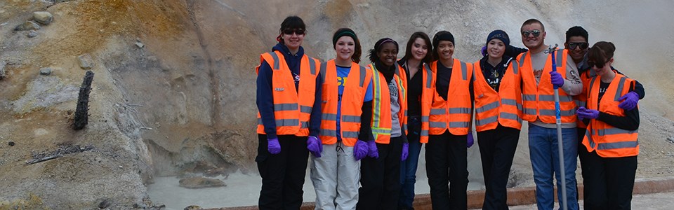 A group of high school students in orange vests in front of a steaming mudpot